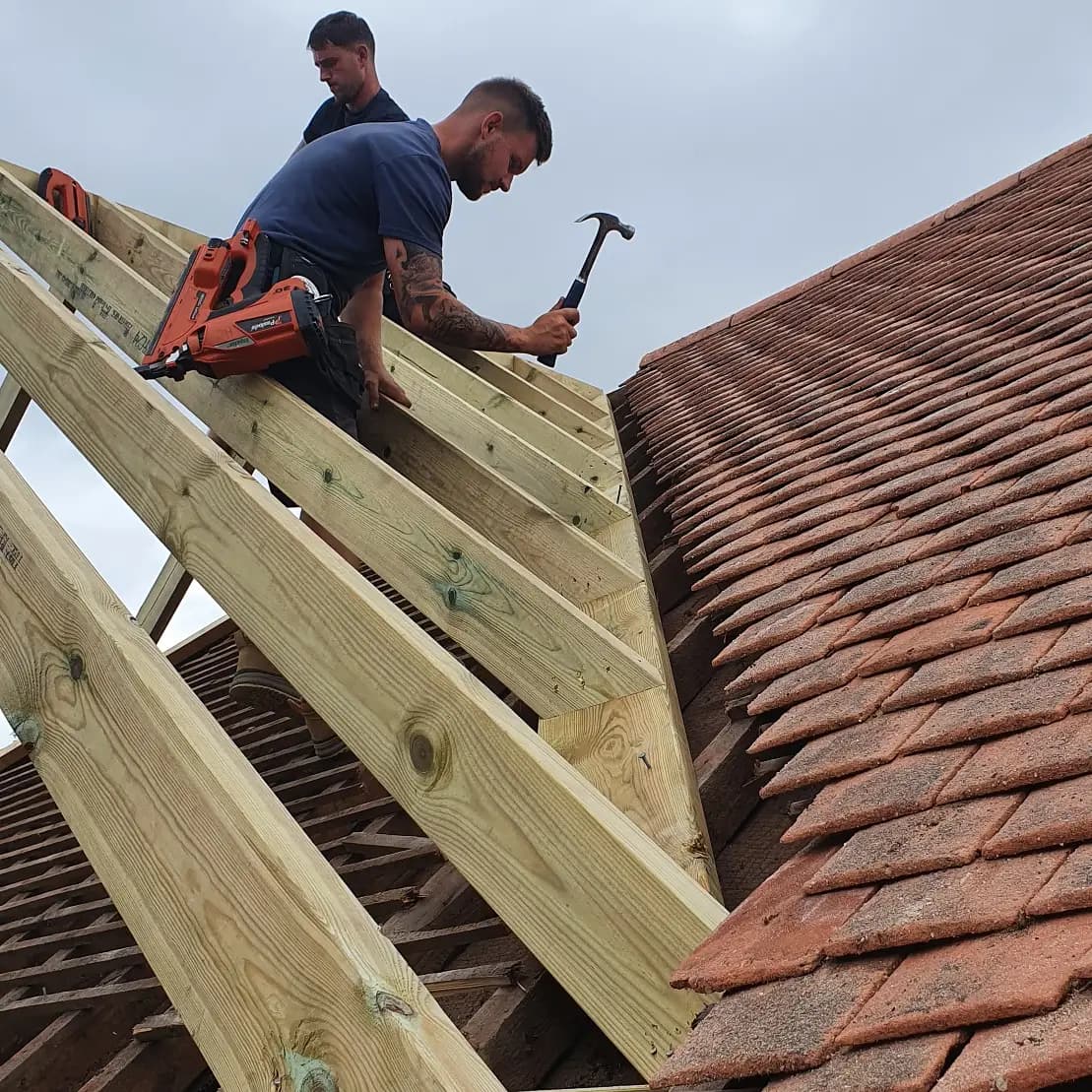 Carpenters fixing new rafters alongside an existing clay tiled roof